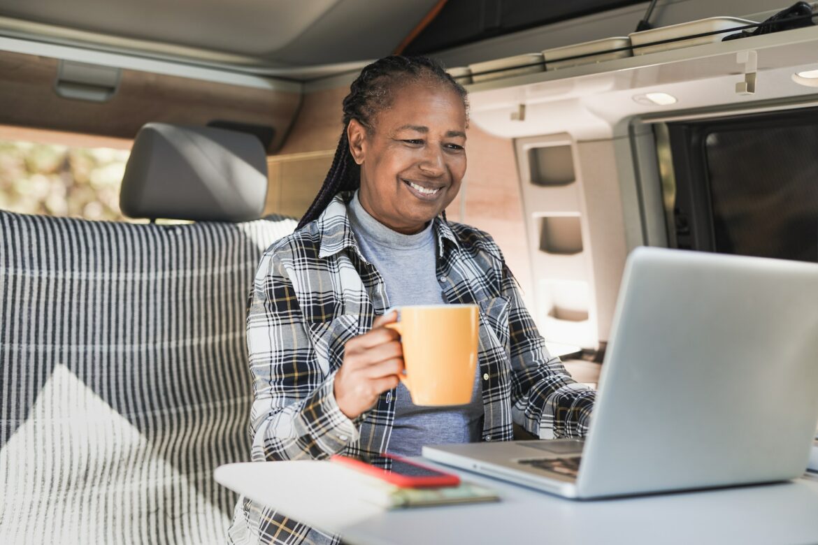 African senior woman using computer laptop inside mini van camper
