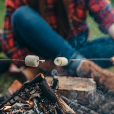 Woman in a blur while holding a marshmallow above the camping fire