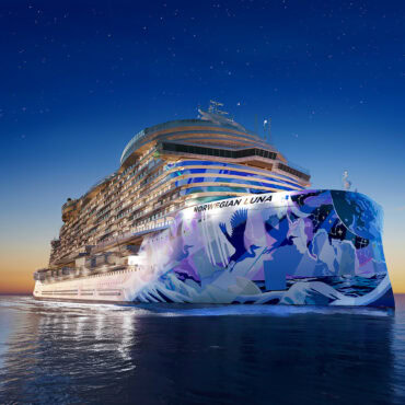 This large ship is your Norwegian Luna cruise. It is depicted sailing on calm waters during twilight. The ship's hull features colorful artwork with abstract designs and bird motifs. The sky is clear with visible stars, transitioning from a deep blue to a warm orange near the horizon.