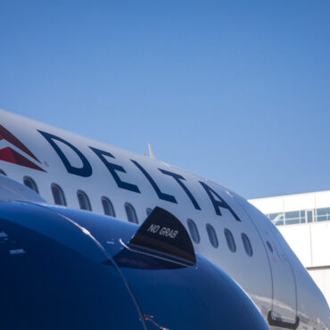 The image shows a close-up of a Delta Air Lines airplane. The Delta logo and name are prominently displayed on the side of the aircraft. Configured with Delta A321neo First Class