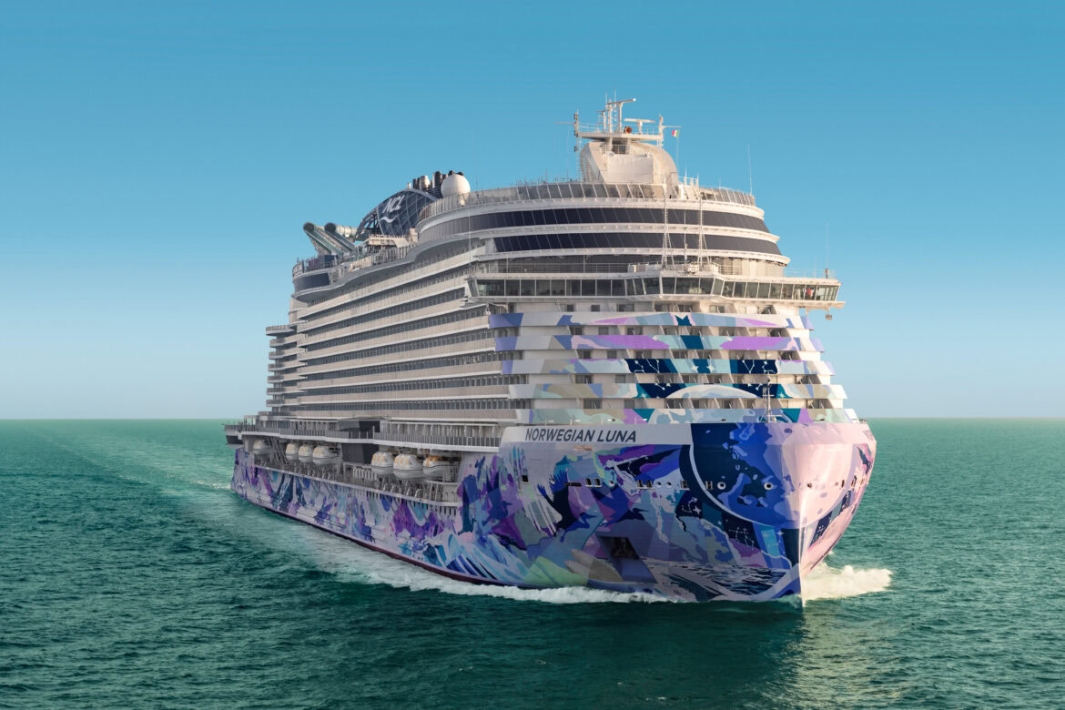 The image shows the Norewegian Luna cruise ship named "Norwegian Luna" sailing on the ocean. The ship features a colorful and artistic design on its hull, with shades of blue, purple, and white. The sky is clear and blue, and the water is calm.